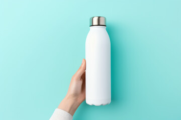 A hand holding a reusable steel stainless eco thermo water bottle on a blue background. This image can be used for a variety of purposes, such as product photography, marketing, and advertising.