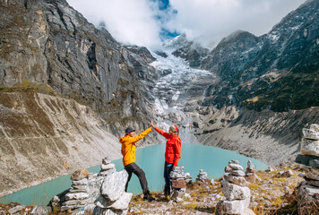 Wall Mural - Trekkers couple dressed bright waterproof jackets giving High Five enjoying glacier falling in high altitude Sabai Tso glacial lake 4350m. Makalu Barun National Park, Mera peak climbing route, Nepal