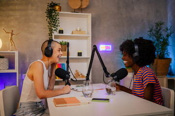 Wall Mural - Two gen z multiracial women are sitting at home recording studio while recording a podcast.