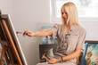 © stivog - Young, blonde woman painting in her atelier