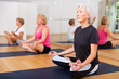 © JackF - Aged woman who cares about her health and does yoga in a group workout, sits in a half-lotus position in a fitness studio