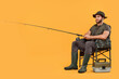 Fisherman with rod and tackle box on chair against yellow background