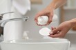 Woman applying makeup remover from bottle onto cotton pad in bathroom, closeup
