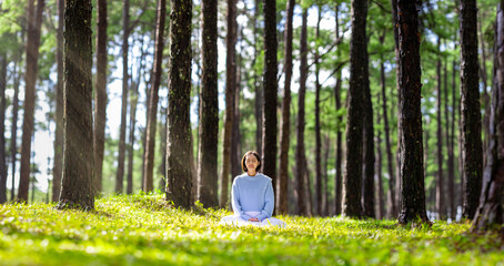 Woman relaxingly practicing meditation in the pine forest to attain happiness from inner peace wisdom with beam of sun light for healthy mind and soul for healthy mind and soul