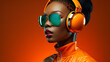 Young african american woman listening to music. High fashion studio portrait of black model with sunglasses, headphones and beautiful makeup on neon orange colourful background, copy space