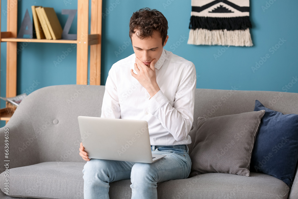 Young man with laptop sitting on sofa at home