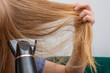 Kobieta suszy długie blond włosy suszarką elektryczną 