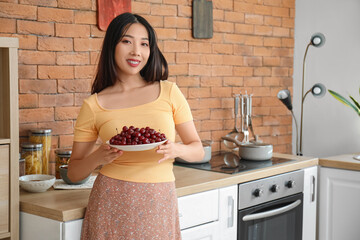 Wall Mural - Happy beautiful young Asian woman with bowl of ripe cherries in kitchen