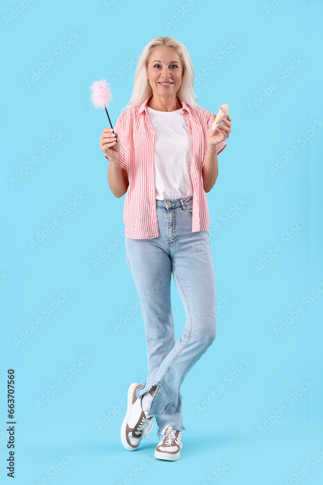 Mature woman with feather stick and vibrator on blue background