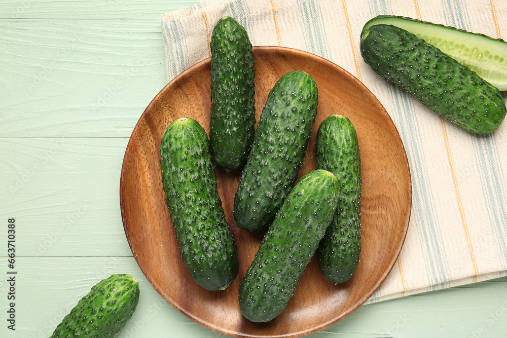 Plate with fresh cucumbers on green wooden background