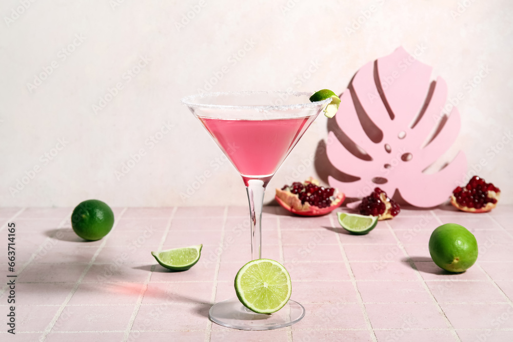 Glass of Cosmopolitan cocktail with lime on pink tile table