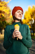A bright atmospheric color portrait of a young woman in a red hat with a bright yellow ice cream in her hands. Autumn walk in the park in good weather.