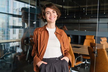 Portrait of young confident woman, start-up manager in office, posing with confidence, looking self-assured, wearing casual, informal clothes