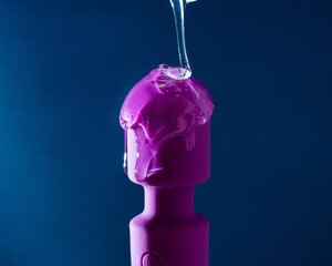 Wall Mural - Intimate lubricant pours on a purple vibrator on a blue background. 