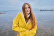 © Iuliia Pilipeichenko - Happy girl in a yellow raincoat walks along the beach of a lake or river on a cool day. Travel concept. Girl on a journey. Amazing scenic street view