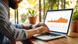 © zeenika - Man sits comfortably with his laptop, engrossed in analyzing a business graph, strategic thinking, he navigates through the data, making informed decisions to drive growth.