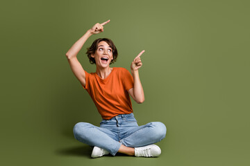 Wall Mural - Full length photo of impressed girl dressed t-shirt sit on floor look directing at promo empty space isolated on green color background