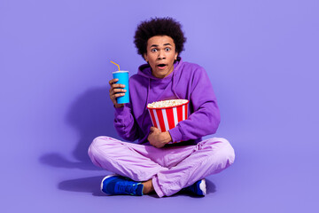 Wall Mural - Full length photo of astonished scared guy dressed violet hoodie watch horror movie with popcorn isolated on purple color background