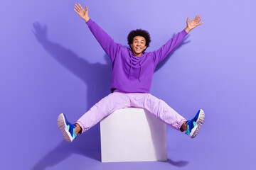 Poster - Full length photo of satisfied positive guy sit on white platform raising hands up announcing sale isolated on violet color background