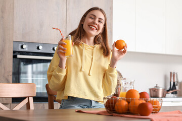 Sticker - Young woman with glass of juice and orange in kitchen