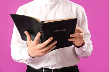 Young man reading Bible on purple background, closeup