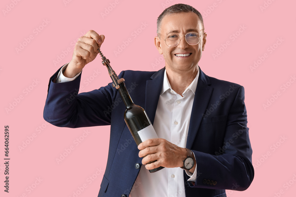Mature man opening bottle of wine on pink background