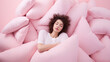 Young woman sleep surrounded by a pile of pillows on a pink pastel background. Creative concept for mattress and pillow store, orthopedic sleep products.