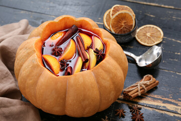 Wall Mural - Tasty mulled wine in pumpkin with ingredients on black wooden background