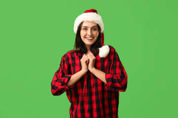 Wall Mural - Beautiful young woman in pajamas and Santa hat on green background