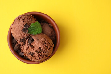 Wall Mural - Bowl of tasty ice cream with chocolate chunks and mint on yellow background, top view. Space for text