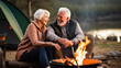 Senior retired couple laughing and talking while cuddling by a campfire in the outdoors