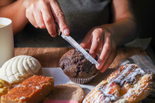 Woman's hand taking a piece of Mexican sweet bread from a white plate on a wooden table. Concept of hands handling food, cutting a chocolate muffin with a knife, front view, horizontal image.