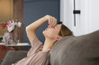 © triocean - Side view of woman with symptoms of frontal sinusitis, feeling of pressure between the eyes sitting on the sofa in the living room