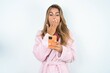 young beautiful woman standing over white studio background being deeply surprised, stares at smartphone display, reads shocking news on website, Omg, its horrible!
