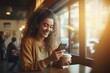 Happy female student sitting outside in a coffee shop, using a smartphone