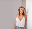 © Dreams Studio™ - Beautiful confident young woman smiling. Leaning against the wall. Female model wearing white top and jeans looking at camera. Studio photography.