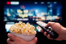 Tv movie night with family. Stream VOD platform. Popcorn and remote control. Video entertainment and snack. Play online film on television. On demand service. Streaming series on digital device.