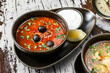 Tasty hodgepodge soup with meat, olives, greens and sour cream on bowl on rustic wooden background. Close up