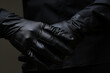 Person wearing black gloves and black jacket with black background.