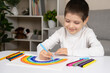 © Zarina Lukash - A small child draws a rainbow with felt-tip pens in a sketchbook while sitting at a table