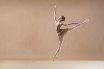 Wall Mural - Beautiful young girl professional student ballerina in pointe shoes and a leotard on a light beige background.