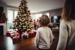 Children with their backs looking at the Christmas tree and gifts and family in the background. Concept of Christmas day or three wise men day.
