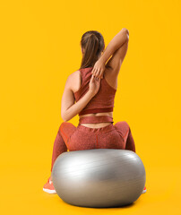 Canvas Print - Sporty young woman training with fitball on yellow background, back view