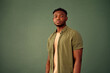 © HBS - Confidence and pride. Front view of african young man with serious facial expression standing over green studio background. Handsome male in casual khaki shirt controlling emotions and mimics.