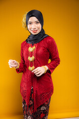 Wall Mural - Muslim woman wearing traditional wear red kebaya and hijab isolated on yellow background. Idul Fitri and hijab fashion concept.