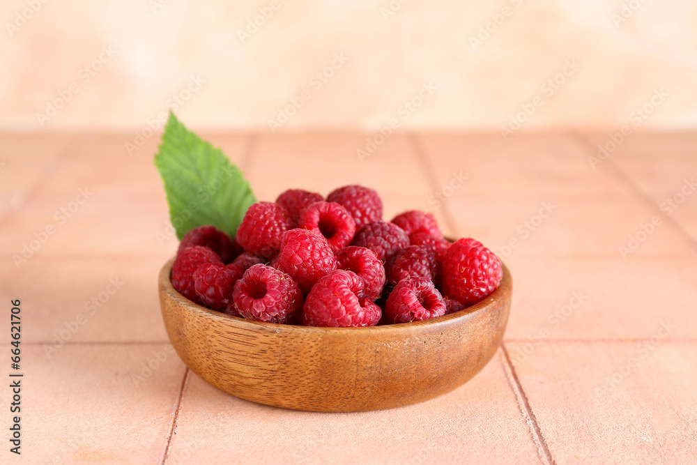 Wooden bowl with fresh ripe raspberries and leaf on pink tile table