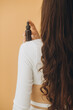 © dsheremeta - A woman holds a bottle of cosmetics in her hand, standing with her back to the camera. Cosmetics mockup.