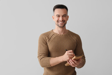 Wall Mural - Happy young man writing in notebook on light background