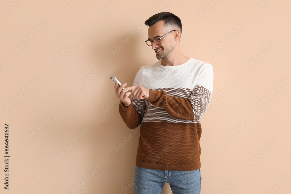 Happy young man using mobile phone on beige background