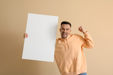 Wall Mural - Happy young man with blank poster on beige background